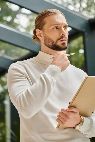 Arquitecto bien parecido enfocado en cuello alto cómodo blanco con barba sosteniendo su papeleo en la puesta en marcha - foto de stock