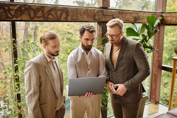Привлекательные концентрированные бизнесмены в элегантных нарядах обсуждают свой проект и держат в руках ноутбук — стоковое фото