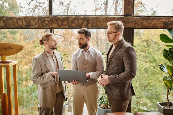 Beaux hommes d'affaires concentrés à la recherche dans des vêtements élégants discuter de leur projet et tenant ordinateur portable — Photo de stock