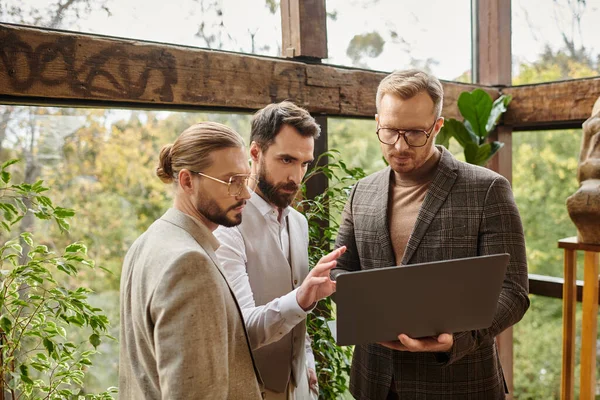 Atractivos empresarios concentrados en trajes elegantes discutiendo su proyecto y la celebración de la computadora portátil - foto de stock