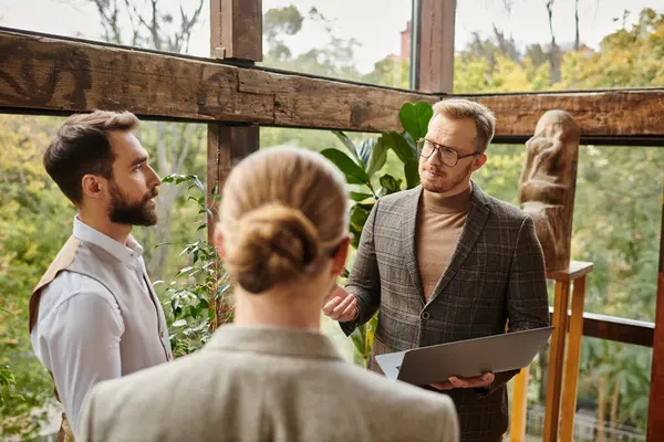 Привлекательные концентрированные бизнесмены в элегантных нарядах обсуждают свой проект и держат ноутбук — стоковое фото