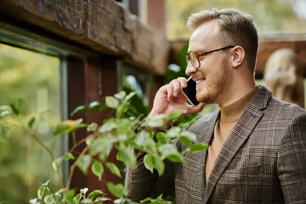 Cheerful handsome man with glasses in sophisticated jacket smiling happily and talking by phone — Stock Photo