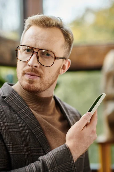 Schöner konzentrierter Führer mit Brille und elegantem Stil, der mit seinem Handy in der Hand posiert — Stockfoto