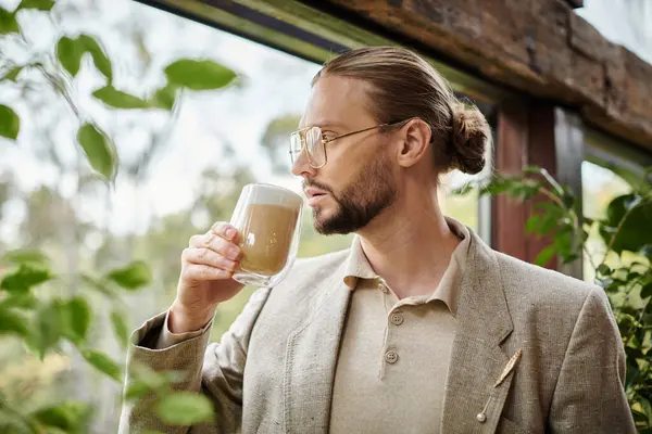 Гарний вигляд привабливого чоловіка з бородою і зібраним волоссям в елегантному костюмі, що п'є свою гарячу каву — стокове фото