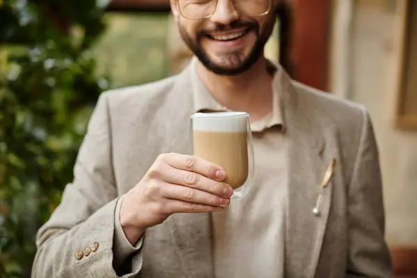 Homem feliz de boa aparência com barba e cabelo coletado em terno elegante desfrutando de seu café quente — Fotografia de Stock
