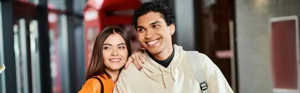 Alegre pareja interracial sonriendo dentro del albergue, aparentemente emocionado por las vacaciones, pancarta - foto de stock