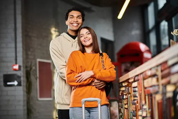 Soddisfatto coppia diversificata in abbigliamento casual abbracciando accanto a un bancone di ostello vicino ai bagagli — Foto stock