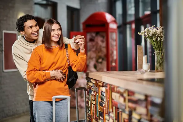 Una donna e un uomo sorridenti stanno insieme alla reception dell'ostello, tenendosi per mano durante il check-in — Foto stock