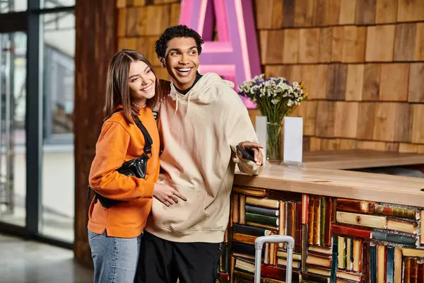Happy diverse couple, dressed in casual clothes standing happily surrounded by shelves of books — Stock Photo