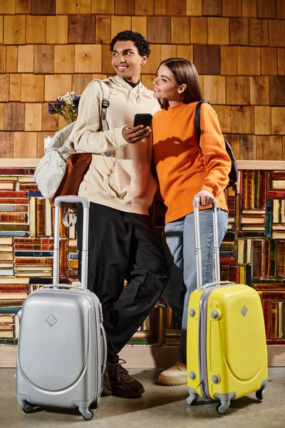 Heureux couple bien habillé se prépare pour leur voyage, entouré de bagages et étagères de livres — Photo de stock