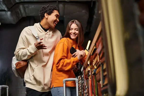Hombre negro feliz hablando con la mujer alegre con tarjeta de crédito en el mostrador de recepción en el albergue - foto de stock