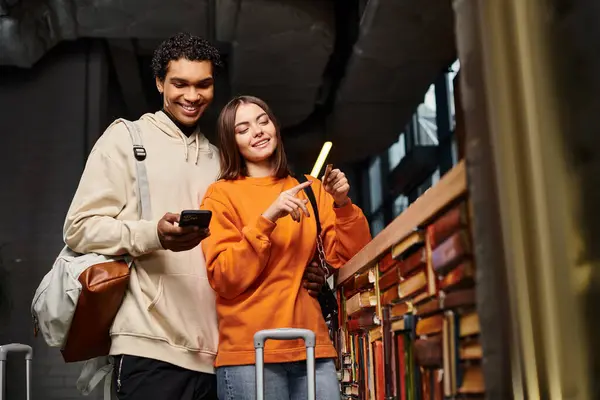 Весела пара зі смартфоном насолоджується часом у гуртожитку з бібліотекою, дивлячись на кредитну картку — стокове фото