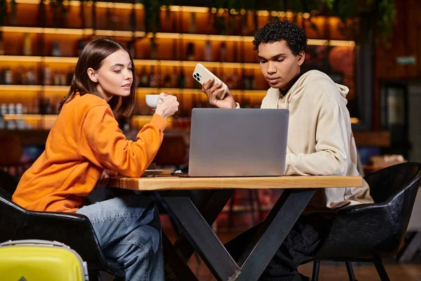 Focused diverse couple using a laptop and smartphone in a modern cafe setting for work or study — Stock Photo