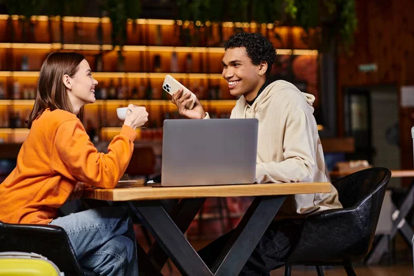 Feliz casal diverso usando um laptop e smartphone em um cenário moderno café para trabalho ou estudo — Fotografia de Stock