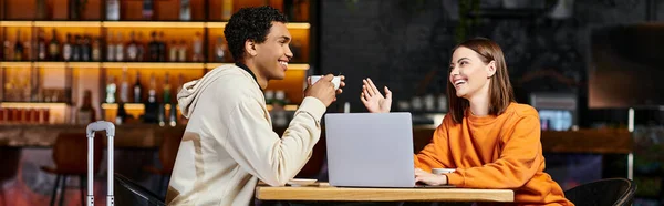 Homme et femme noirs riant et parlant à une table de café, avec leur ordinateur portable à côté d'eux, bannière — Photo de stock