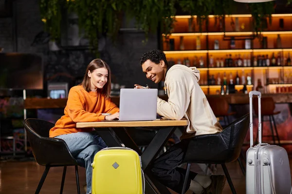 Black man and woman looking at laptop on cafe table, with their luggage beside them, travel — Stock Photo