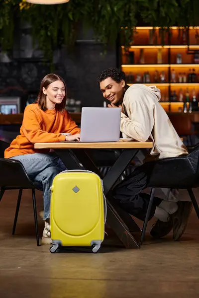 Noir homme et femme regardant ordinateur portable sur la table de café, avec leurs bagages à côté d'eux, nomade numérique — Photo de stock