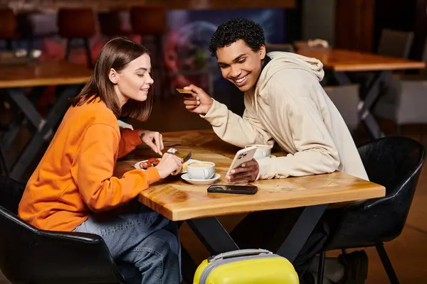 Разнообразная пара, занимающаяся контентом на смартфоне в кафе и обедающая, делающая онлайн покупки — стоковое фото