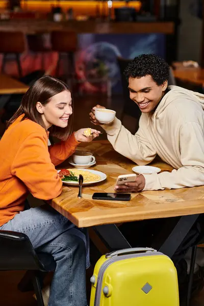 Diversa pareja mirando el teléfono inteligente sobre el café, hombre negro y mujer bonita en la cafetería albergue - foto de stock