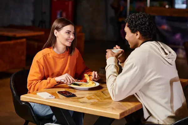 Interracial couple enjoying romantic meal at a cozy wooden table in a bustling restaurant — Stock Photo