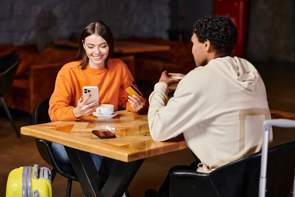 Diverse couple enjoying coffee in cafe, woman holding smartphone and credit card while paying online — Stock Photo