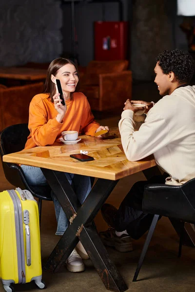 Black man and woman using smartphone while sitting at table with coffee in cafe, luggage and travel — Stock Photo
