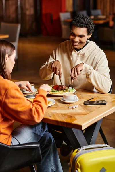 Coppia diversificata che pranza in un ristorante, i loro volti illuminati dalla gioia mentre si godono il cibo gustoso — Foto stock