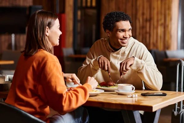 Happy diverse couple enjoying coffee and meal at a rustic wooden table in charming restaurant — Stock Photo