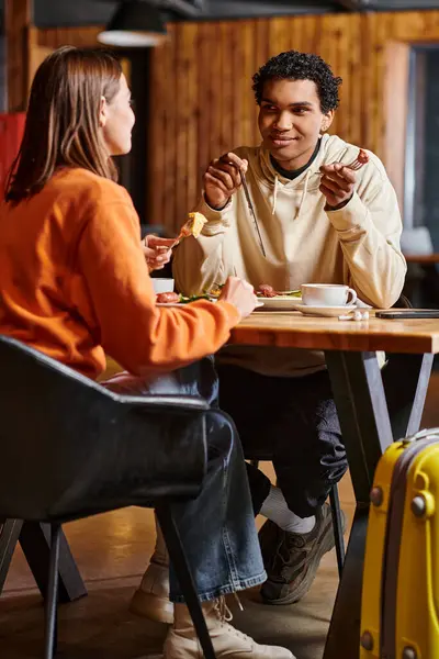 Felice coppia diversificata godendo gustoso pranzo in un tavolo di legno rustico in un ristorante affascinante — Foto stock