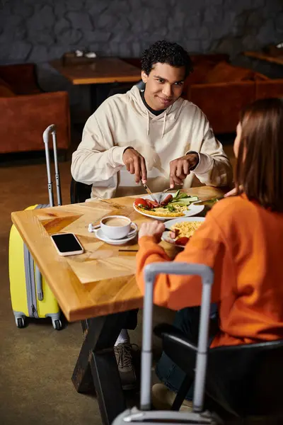 Un hombre y una mujer se sientan en una acogedora mesa, mientras disfrutan de una deliciosa comida juntos en la cafetería - foto de stock