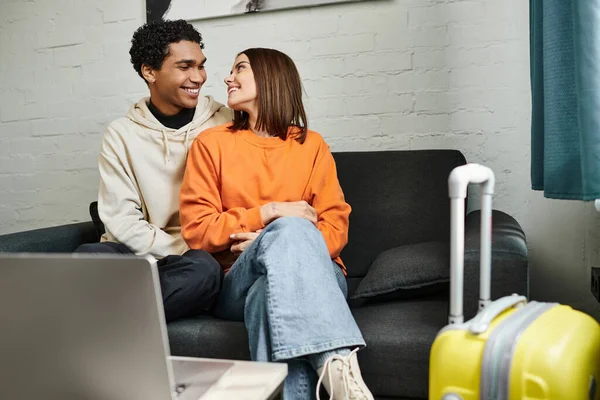Positive multiethnic couple relaxing on a couch in their stylish living room near laptop on table — Stock Photo