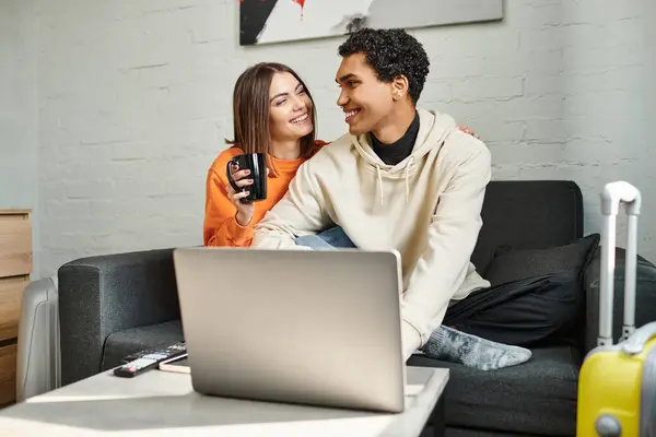Couple interracial insouciant partage un moment confortable comme ils sont assis sur le canapé et en utilisant un ordinateur portable, auberge — Photo de stock