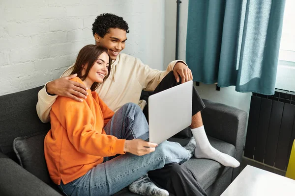 Happy couple snuggled on couch with their faces illuminated by the glow of the laptop screen, movie — Stock Photo