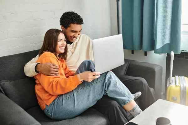 Diverse couple snuggle on couch with their faces illuminated by the glow of the laptop screen, movie — Stock Photo