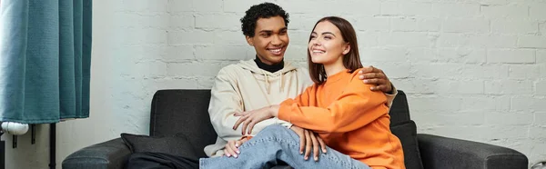 Alegre casal diverso goza de momento acolhedor em um sofá em albergue, viagens e conceito de conforto — Fotografia de Stock