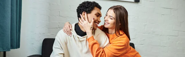 Smiling diverse couple sitting on sofa, woman touching face of black boyfriend, banner — Stock Photo