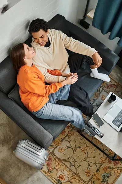 Loving couple enjoys a calm moment while relaxing on sofa with a smartphone, laptop and luggage — Stock Photo