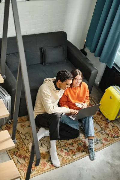 Paar genießt einen gemeinsamen Moment beim Blick auf einen Laptop, während es auf Teppich in der Nähe von Treppen sitzt — Stockfoto