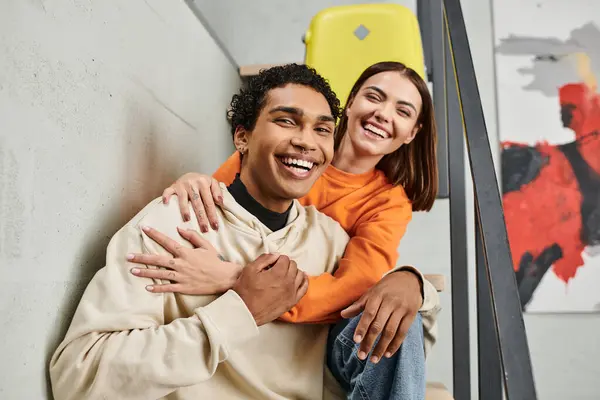 Cheerful interracial couple in casual attire against a backdrop of a brick wall in hostel — Stock Photo