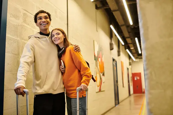 Fröhliches multikulturelles Paar mit Gepäck und Smartphone, das sich in der Herberghalle umarmt, checkt ein — Stockfoto