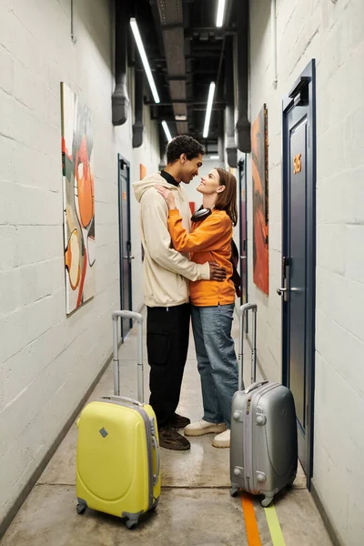 Intimate moment between young multicultural couple facing each other near luggage in hostel corridor — Stock Photo