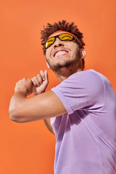 Jovem homem ativo afro-americano gesticulando e sorrindo em fundo laranja, movimento dinâmico — Fotografia de Stock