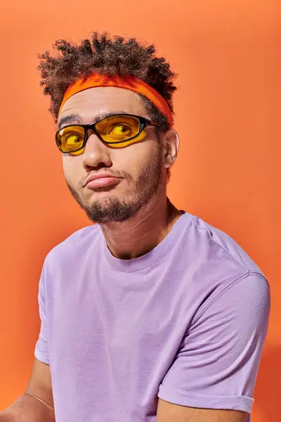 Confused african american fella in eyeglasses and headband looking away on orange background — Stock Photo