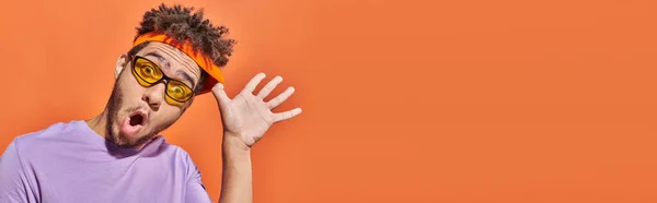 Pancarta, hombre afroamericano con expresión de cara sorprendida ajustando diadema sobre fondo naranja - foto de stock