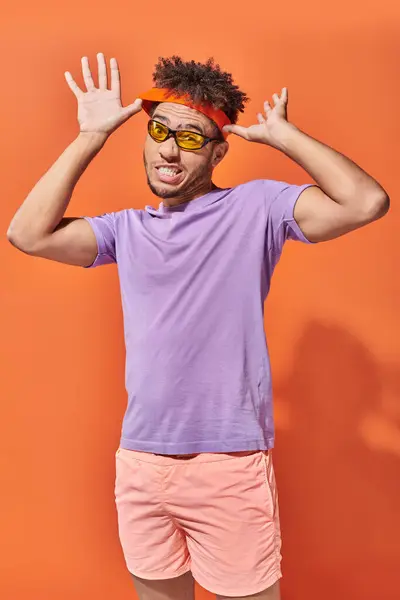 Молодий афроамериканський чоловік в сонцезахисних окулярах, регулюючий пояс на помаранчевому фоні, експресивне обличчя — стокове фото