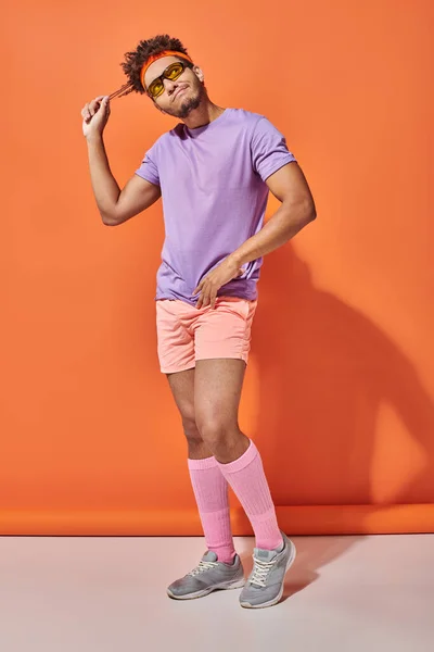 Pensoso sportivo afroamericano in occhiali da sole e abbigliamento da palestra pensando su sfondo arancione — Foto stock
