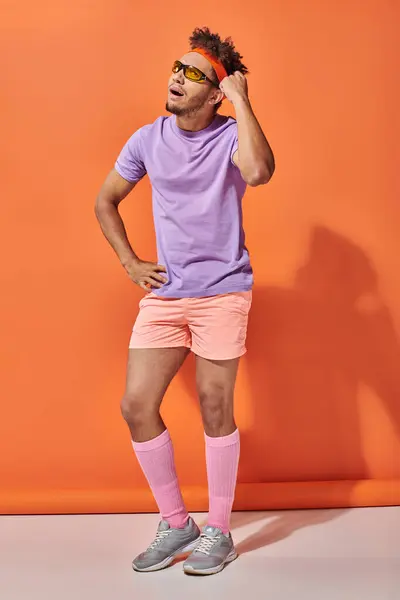 Sportif afro-américain réfléchi en lunettes de soleil et tenue de gymnastique penser sur fond orange — Photo de stock