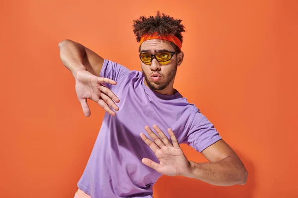 Expressive african american man in eyeglasses and headband gesturing on orange background — Stock Photo