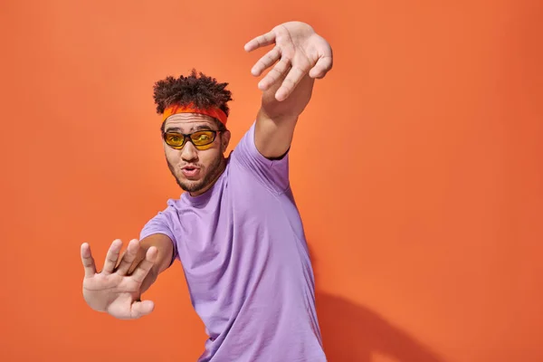 Funny and expressive african american man in eyeglasses and headband gesturing on orange background — Stock Photo