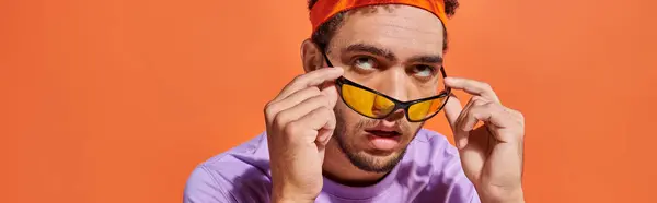 Annoyed african american man in eyeglasses and headband rolling eyes on orange background, banner — Stock Photo